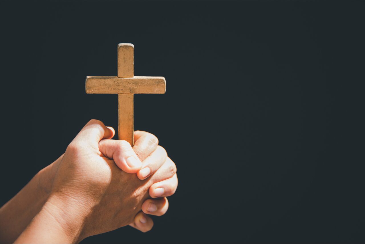 A person praying with clasped hands in front of a cross during a life crisis.